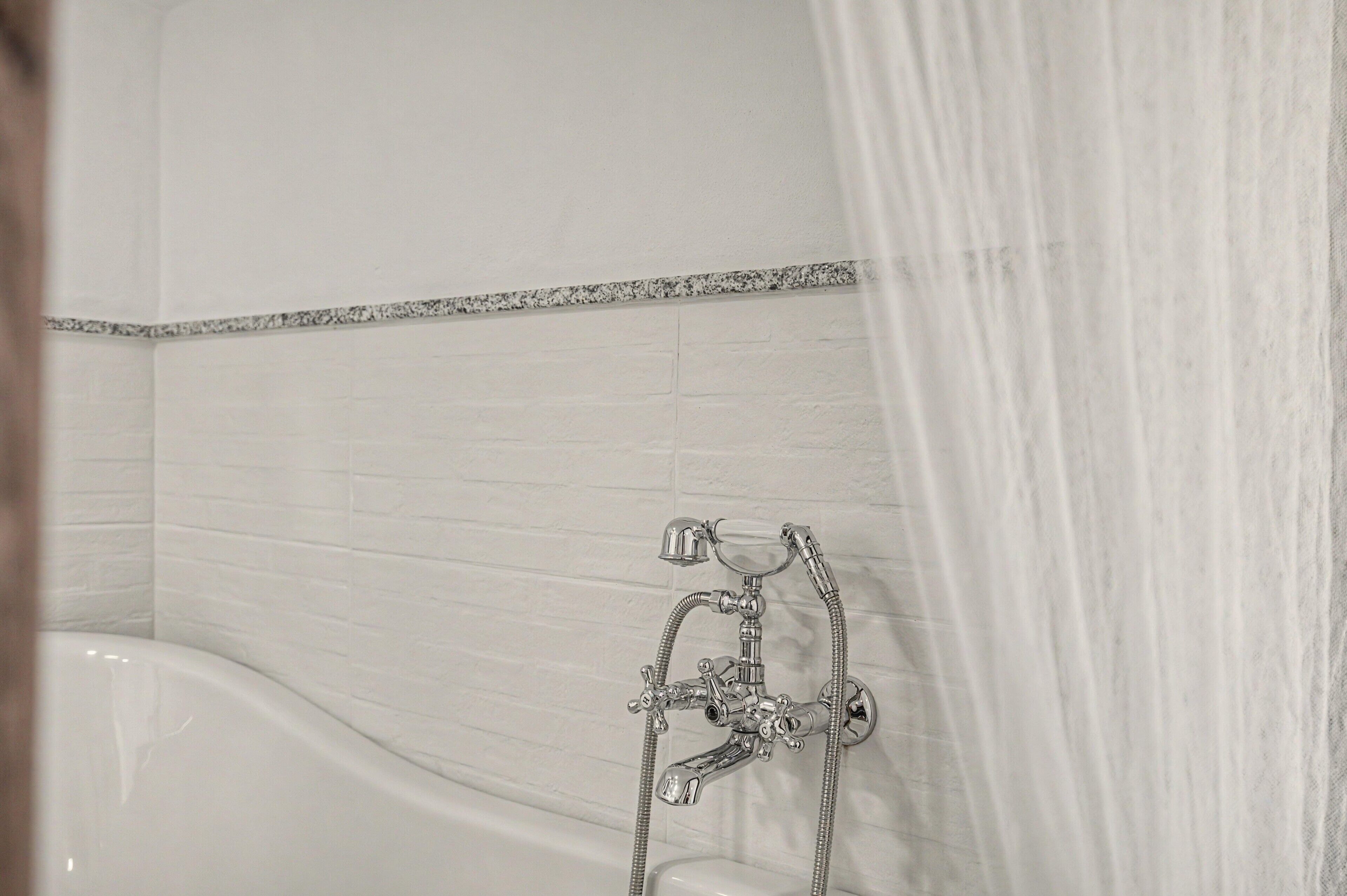 Une salle de bain avec une baignoire, une douche dotée d’un robinet chromé et un mur recouvert de carreaux blancs.