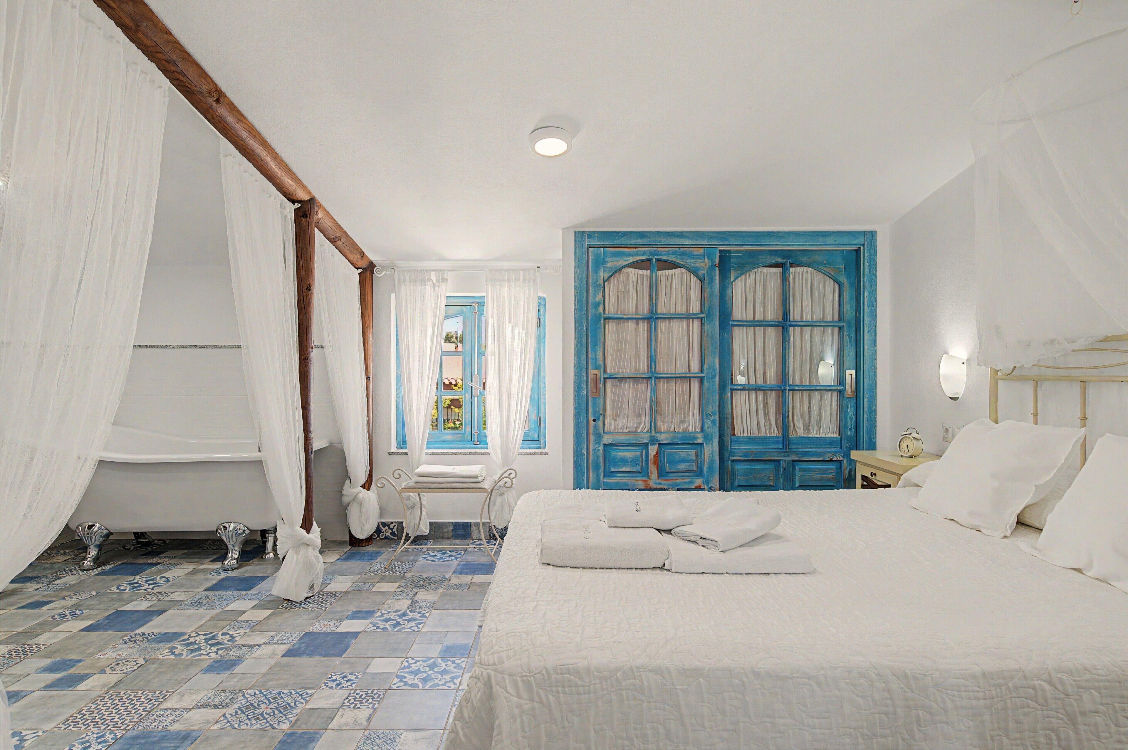A bedroom with a bed, a nightstand, a window with curtains, and a blue door.