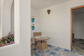 A small outdoor seating area with a round table and wicker chairs, two potted plants on the wall, and a patterned tile floor. - Charming Apartment with Pool, Terrace, Air Conditioning and Wi-Fi (Conil)