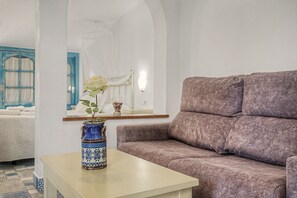 A living room with a sofa, a table with a vase, and a mirror reflecting a window.