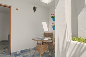 A small, enclosed outdoor seating area with a wicker table and chairs, a potted plant, and a wall-mounted light fixture.
