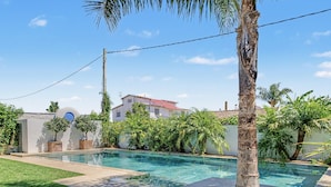 A swimming pool with a clear blue water surface, surrounded by a well-maintained lawn and palm trees. - Charming Apartment with Pool, Terrace, Air Conditioning and Wi-Fi (Conil)