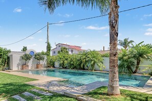 A swimming pool with a clear blue water surface, surrounded by a well-maintained lawn and palm trees.