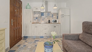 A compact kitchen with white cabinets, a microwave, and a coffee maker. There is a wooden door and a brown sofa in the living area. - Charming Apartment with Pool, Terrace, Air Conditioning and Wi-Fi (Conil)