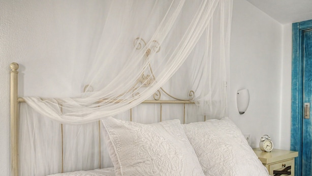 A bed with a canopy, pillows, and a bedside table with a clock. - Charming Apartment with Pool, Terrace, Air Conditioning and Wi-Fi (Conil)