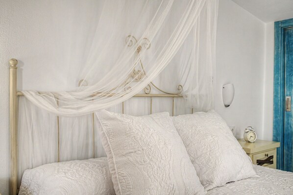 A bed with a canopy, pillows, and a bedside table with a clock.