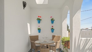 A small outdoor seating area with a round table and wicker chairs, surrounded by white walls and blue patterned tiles. - Charming Apartment with Pool, Terrace, Air Conditioning and Wi-Fi (Conil)