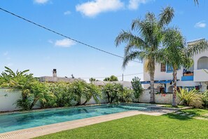 A swimming pool surrounded by lush greenery and a white building with blue accents.