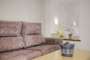 A room with a brown sofa, a table with a decorative vase, and a bed with a white canopy in the background. - Charming Apartment with Pool, Terrace, Air Conditioning and Wi-Fi (Conil)