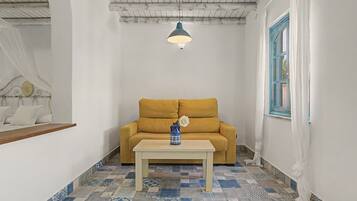 Una habitación con un sofá amarillo, una mesa blanca y un jarrón azul con una flor blanca.