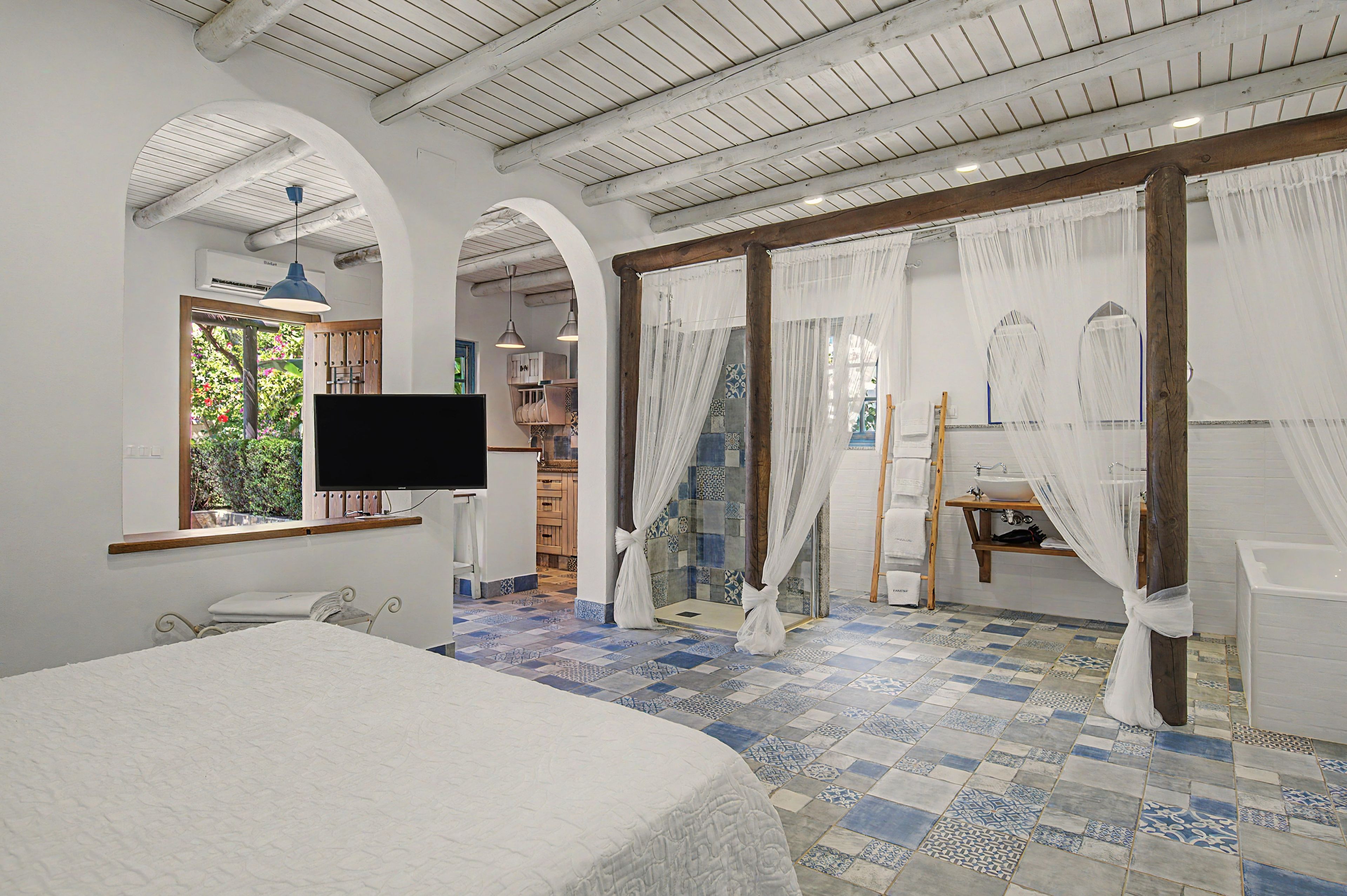 Une chambre à coucher comprenant un lit, une télévision, une fenêtre donnant sur un espace verdoyant, ainsi qu’une salle de bain avec une baignoire et une douche.