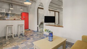 A modern kitchen with a red refrigerator, white bar stools, a TV mounted on the wall, and a patterned tile floor.