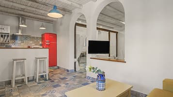 Une cuisine moderne avec un réfrigérateur rouge, des tabourets de bar blancs, un téléviseur fixé au mur et un sol carrelé à motifs.