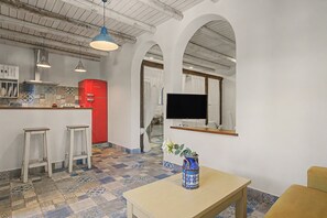 A modern kitchen with a red refrigerator, white bar stools, a TV mounted on the wall, and a patterned tile floor.