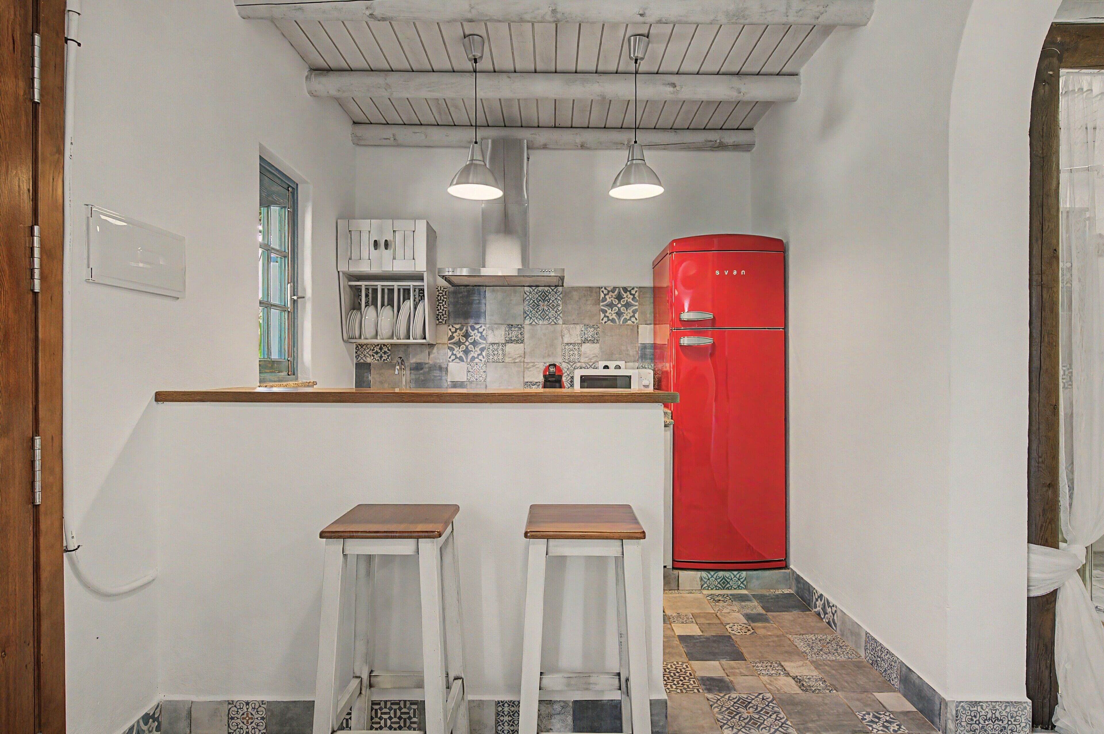 Une cuisine compacte avec un réfrigérateur rouge, deux tabourets de bar et une fenêtre donnant sur un beau paysage.