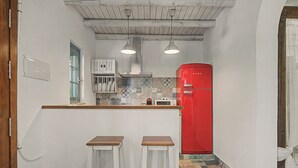 A compact kitchen with a red refrigerator, two bar stools, and a window with a view.