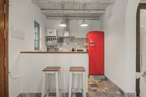 A compact kitchen with a red refrigerator, two bar stools, and a window with a view.