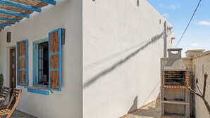 A white building with blue shutters, a stone patio, and a brick oven.