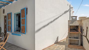 Un bâtiment blanc avec des volets bleus, une terrasse en pierre et un four en briques.