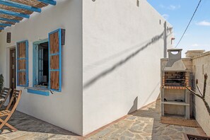 A white building with blue shutters, a stone patio, and a brick oven.
