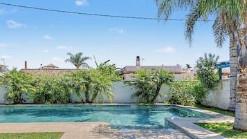 Une piscine à l’eau d’un bleu cristallin, entourée d’une pelouse et de diverses plantes tropicales.