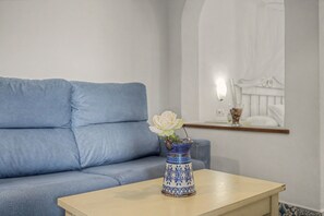 Une pièce avec un canapé bleu clair, une petite table sur laquelle est posé un vase de fleurs blanches, et un élément décoratif mural.
