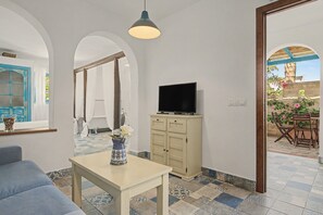 A room with a television on a cabinet, a table with a vase, and a blue sofa.