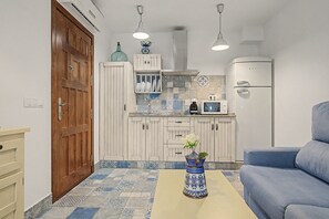 A compact kitchen with a wooden door, white cabinets, a microwave, and a blue sofa.