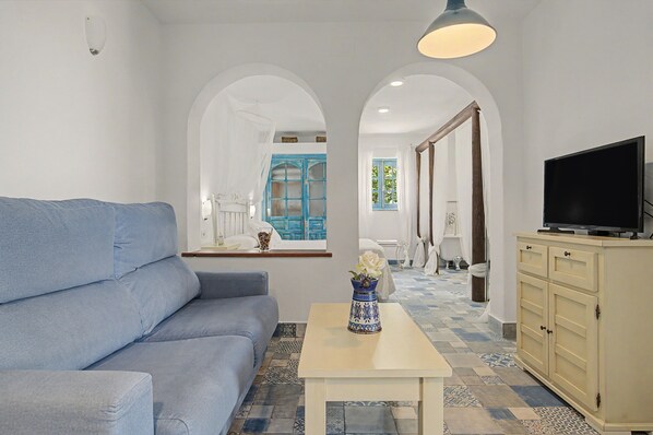 A living room with a sofa, a coffee table with a vase, a television on a cabinet, and a view through an arched doorway.