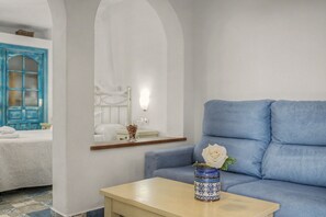 A room with a blue sofa, a small table, a vase with a flower, and a bed with a blue door.
