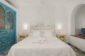 A neatly made bed with white linens and pillows, a bedside table with a clock, and a wall-mounted light fixture.