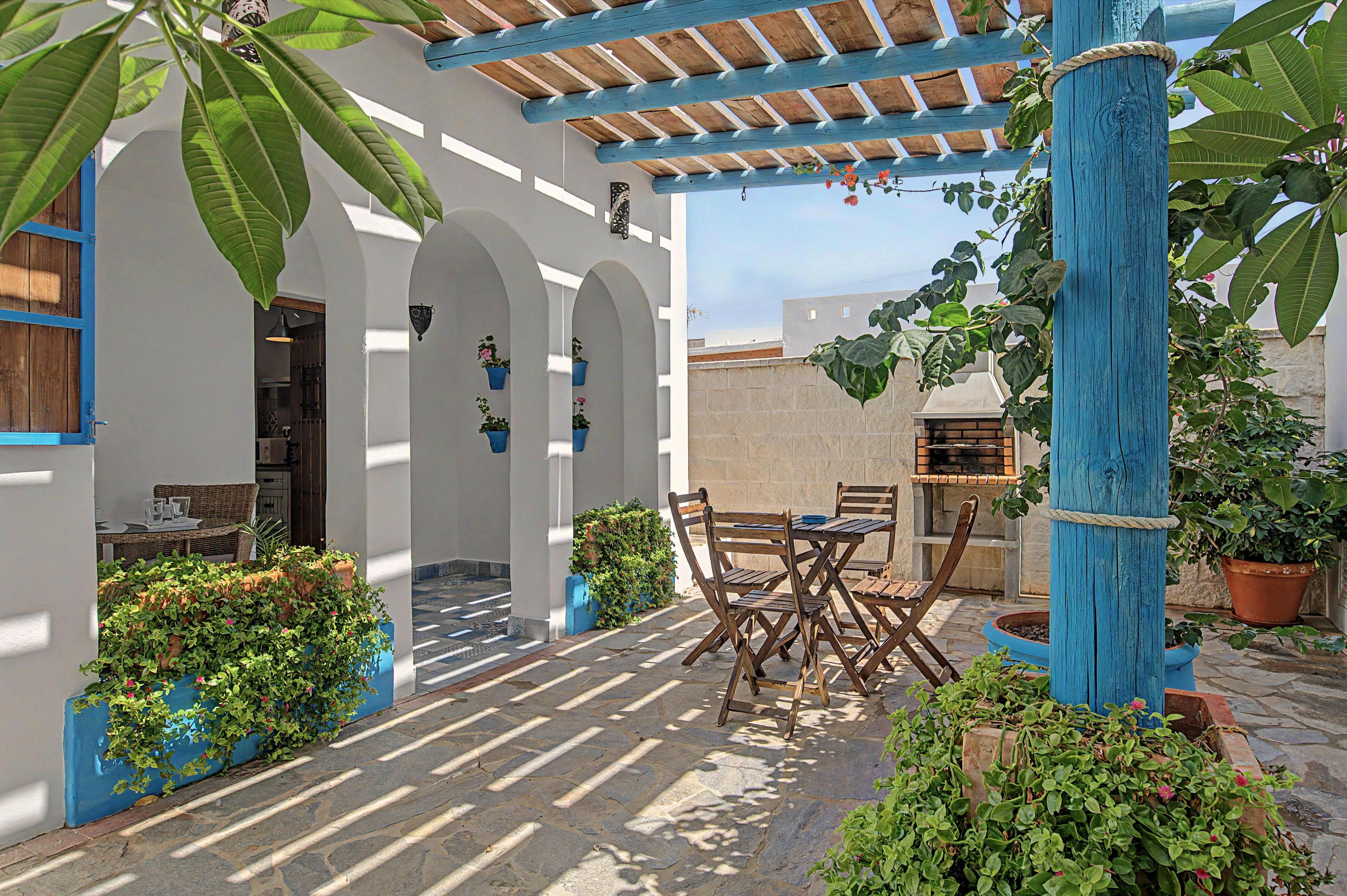 Une cour avec une table et des chaises en bois, des plantes en pot et une structure en bois bleue.