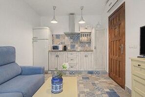 A compact living space with a sofa, a coffee table with a vase, a kitchen area with a microwave, and a wooden door.