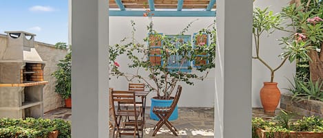 Un patio abrité avec une table et des chaises en bois, une plante en pot et un mur en pierre.