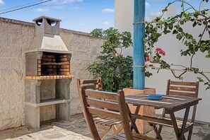 An outdoor seating area with a brick-built barbecue grill, wooden chairs, and a table.