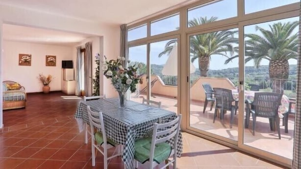 Ein geräumiges Wohnzimmer mit Balkon, einem Esstisch und Blick auf Palmen.