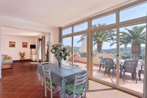 Un vaste espace de vie avec balcon, une table à manger et une vue sur les palmiers.