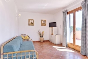 Une chambre avec un lit, une télévision, une petite table avec un vase et une fenêtre avec des rideaux.