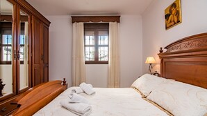 Una habitación de hotel con una cama grande, un cabecero de madera, una mesita de noche con lámpara, un armario y una ventana con cortinas.