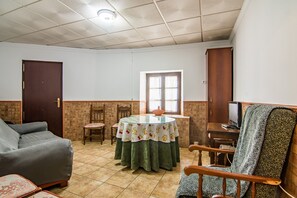 A living room with a sofa, a round table with a tablecloth, a television, and a patterned chair.