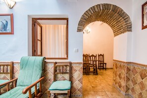A room with a seating area, a dining table with chairs, and an arched doorway leading to another room.