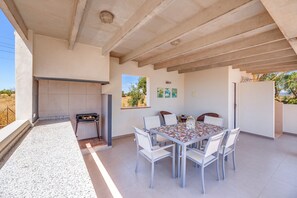 Une terrasse couverte avec un barbecue, une table à manger avec des chaises et une vue sur l’extérieur.
