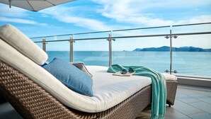 A balcony with a wicker sofa, pillows, a book, and glasses, overlooking a body of water and distant land. - Signiel Busan (Busan)