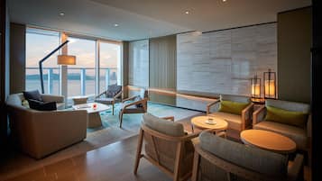 A modern living room with a large window overlooking a body of water, furnished with sofas, chairs, and a coffee table.
