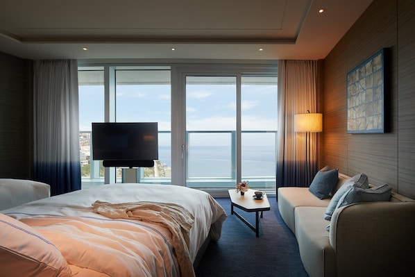 A hotel room with a large bed, a sofa, a small table, a TV, and a view of the sea through large windows. - Signiel Busan (Busan)