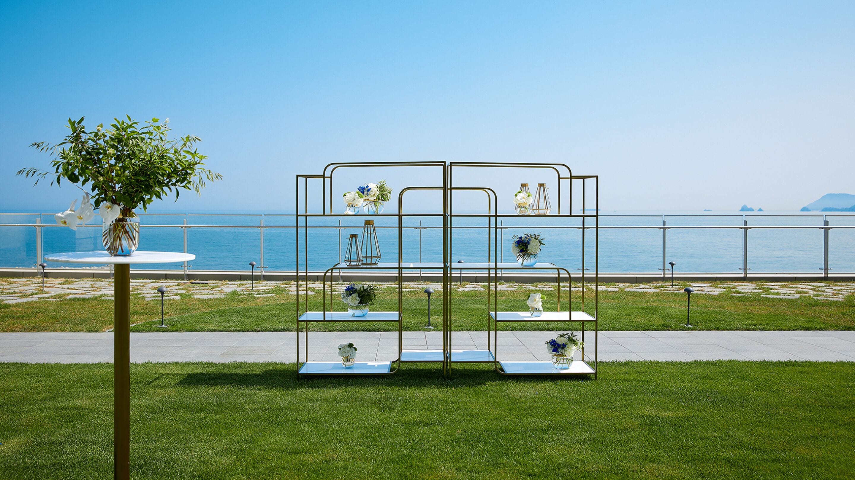 A seaside outdoor seating area with a metal structure, tables, and chairs, overlooking the ocean.