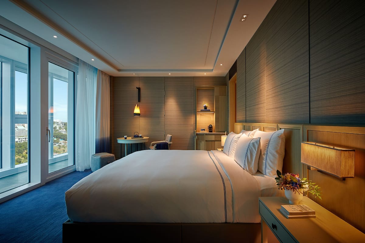 A modern hotel room with a large bed, a desk, and a view of the city.