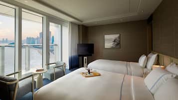 Une chambre d’hôtel avec deux lits, une télévision, une petite table avec un plateau, et une vue sur un paysage urbain et une étendue d’eau.