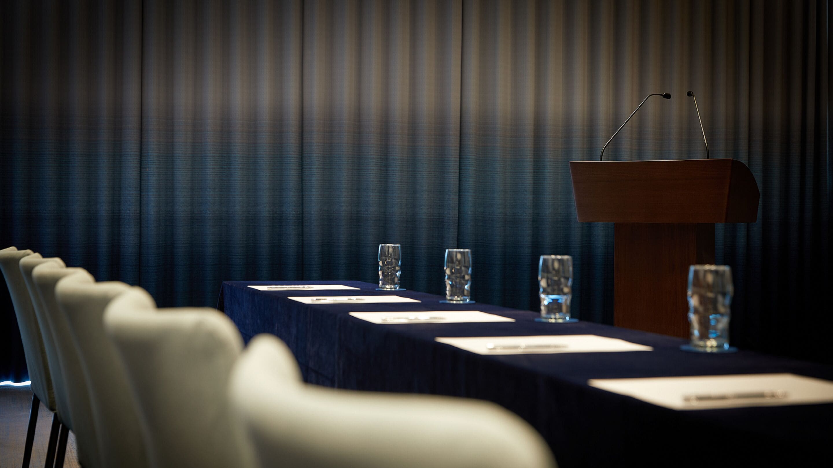 A conference room with a long table, chairs, a podium, and glasses.