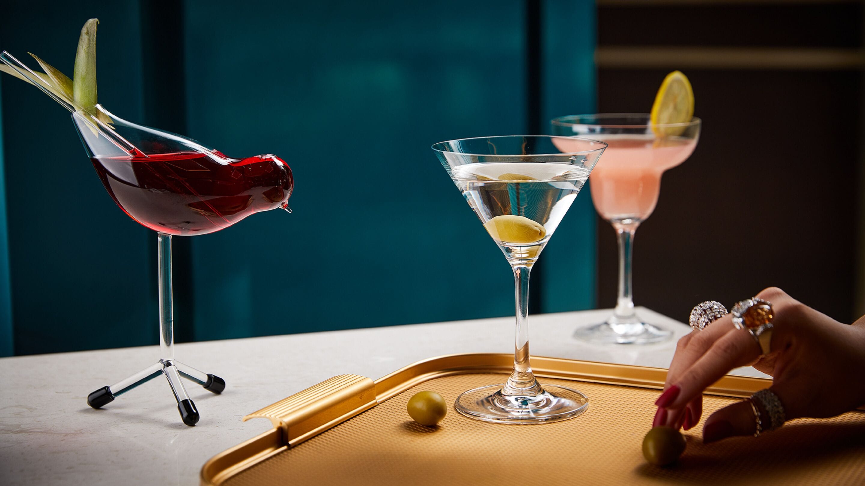 Three martini glasses on a tray with olives, a feather, and a lemon slice.